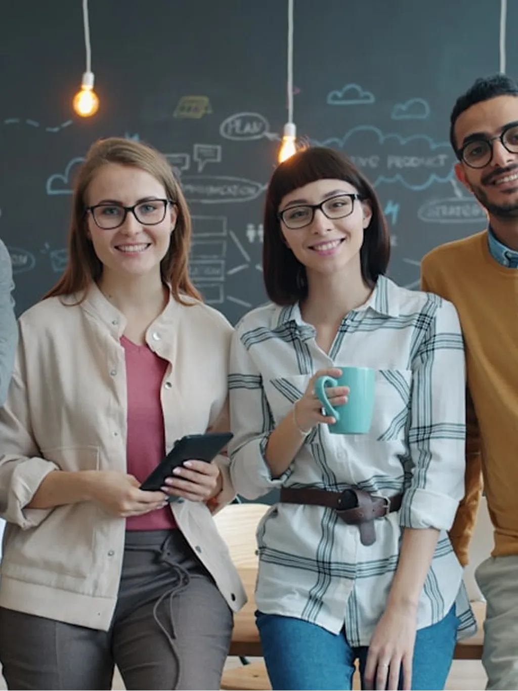 A group of young people stands in front of a chalkboard, engaged in discussion and sharing ideas.